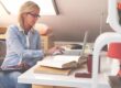 Woman working on a laptop at a desk with books in a bright attic office space.
