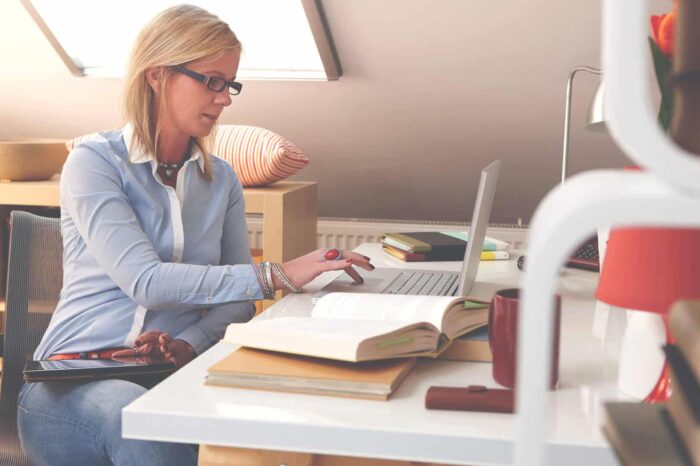 woman_4 Woman working on a laptop at a desk with books in a bright attic office space.